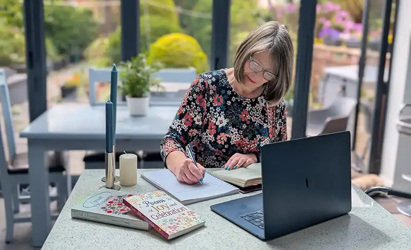 Woman writing in notebook at desk with laptop.
